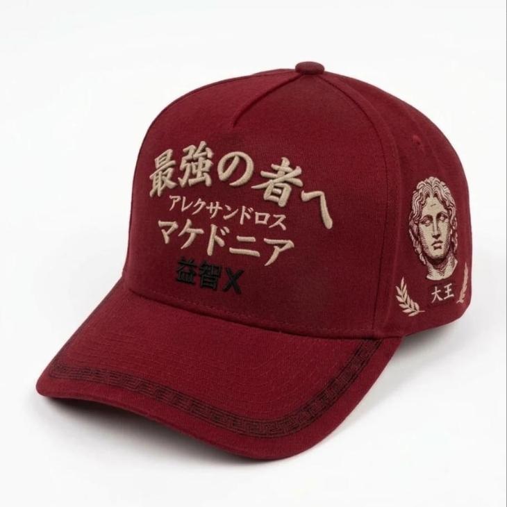 Gorra roja con el frente anterior: 最強の者へ en arco, アレクサンドロス, マケドニア y 益智X en negro